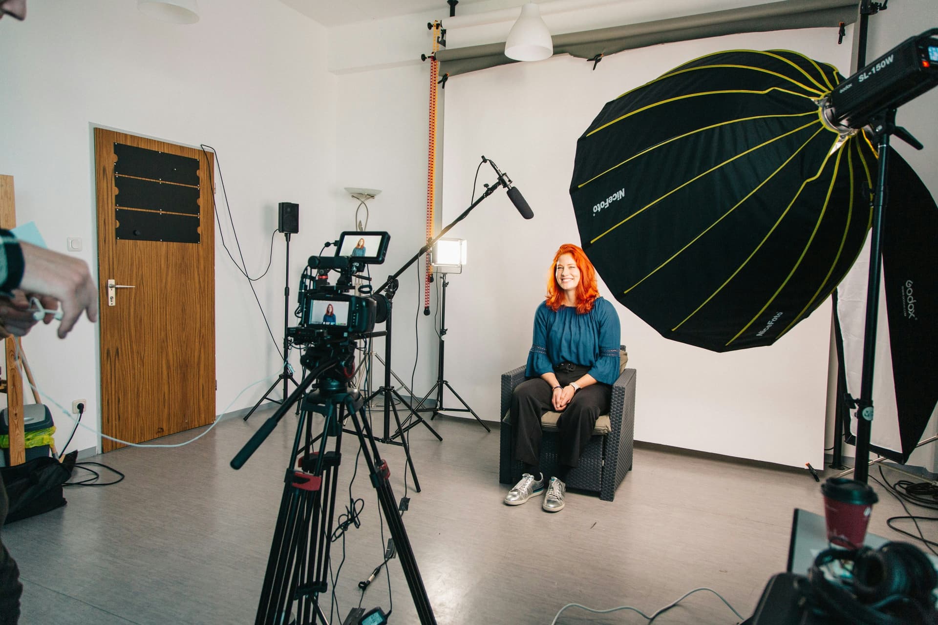 Video production setup with camera gear, lighting equipment, and a microphone boom, preparing to photograph person sitting down.