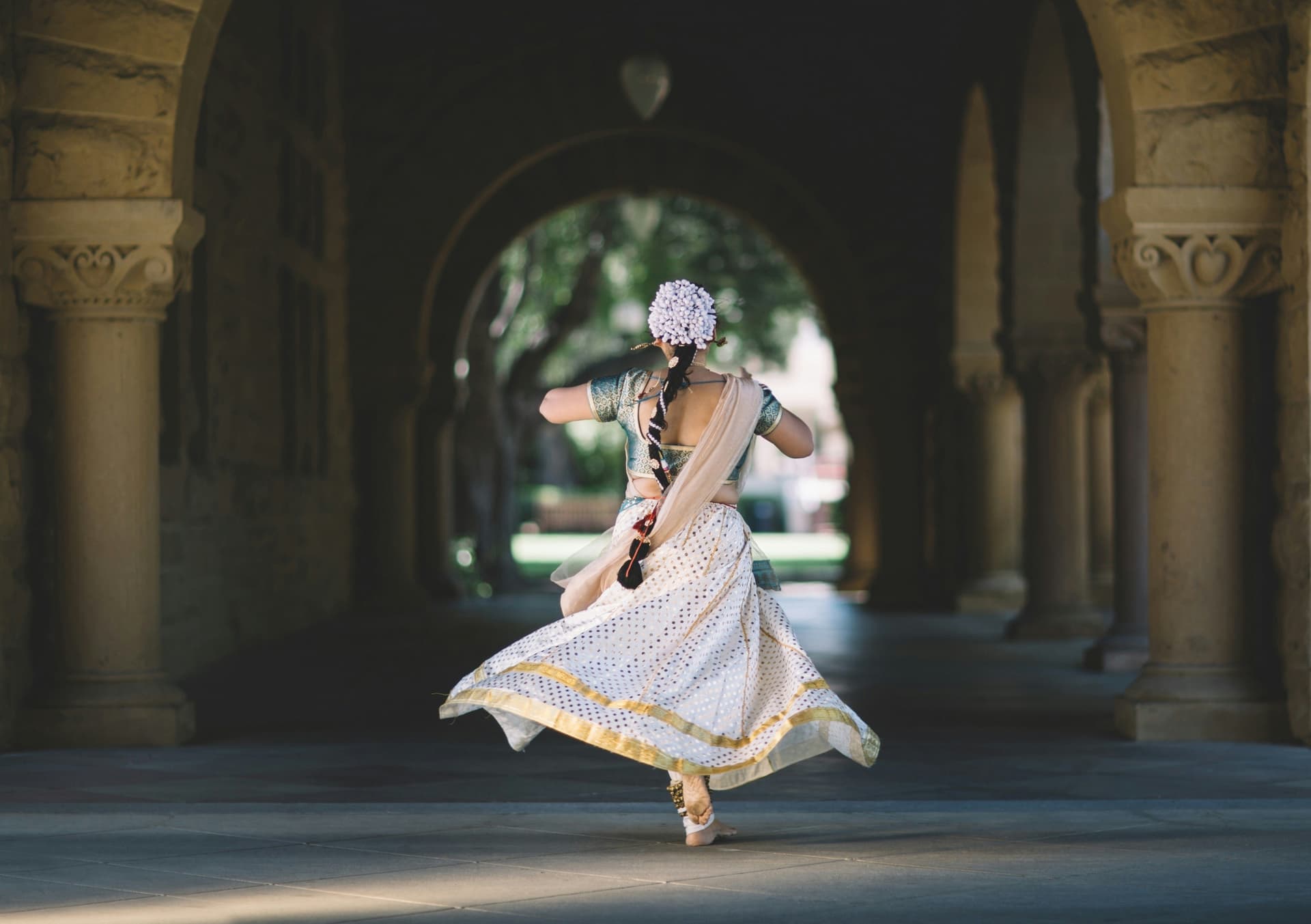 Woman in traditional Indian dress twirling under an arched hallway.